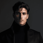 A man with tousled dark hair wears a high-collared black coat and a turtleneck, standing against a dark background, exuding a sophisticated and mysterious aura.
