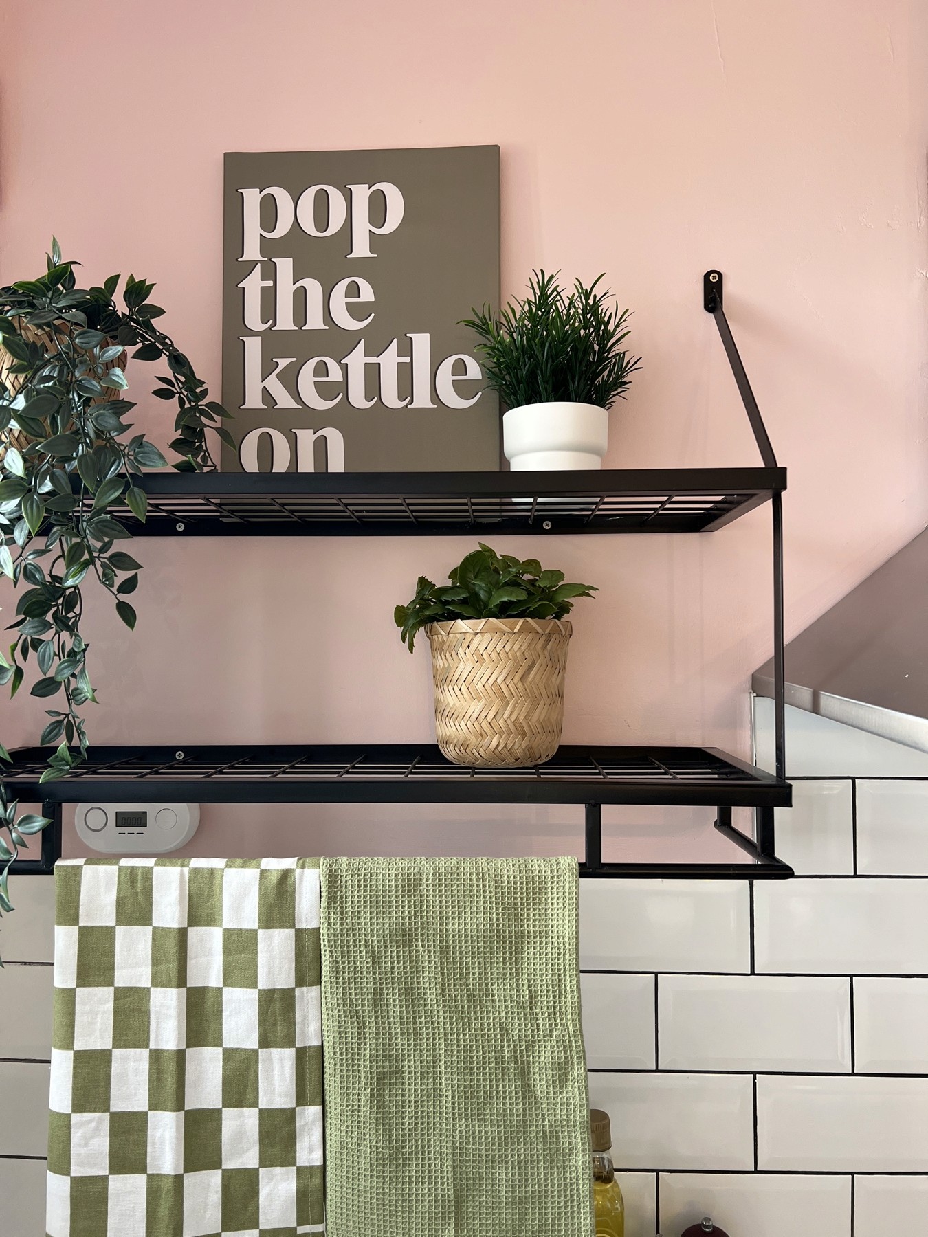 Kitchen shelf with a Pop The Kettle On print, houseplants and green checked tea towels