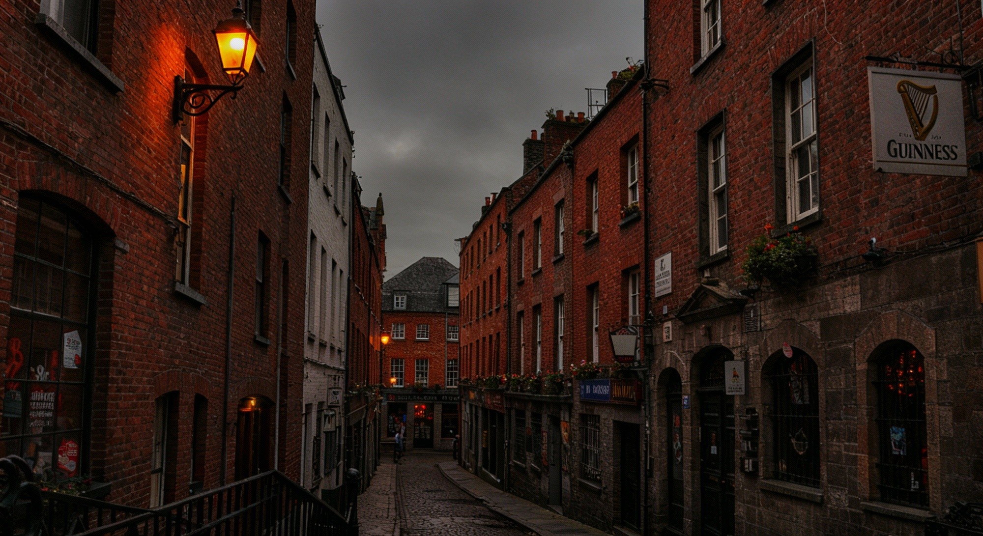 A moody dusk photograph of a narrow cobblestone alleyway lined with red brick Georgian buildings and a glowing street lamp, evoking an atmospheric European city streetscape.