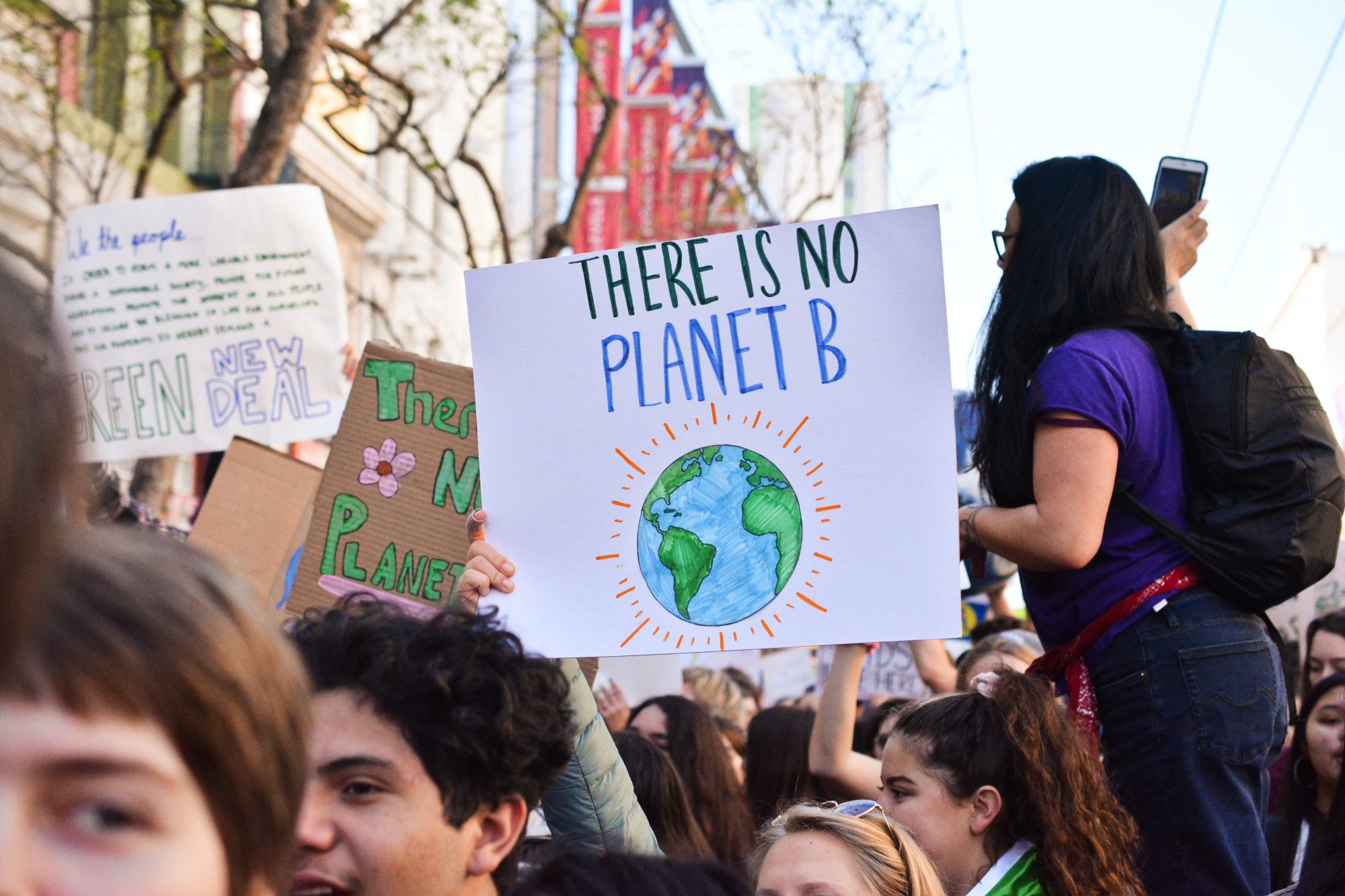 A crowd at a protest, with a person holding a sign featuring a drawing of the Earth.