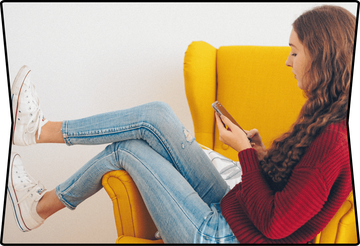 a young woman sitting on a yellow sofa while looking at her smartphone