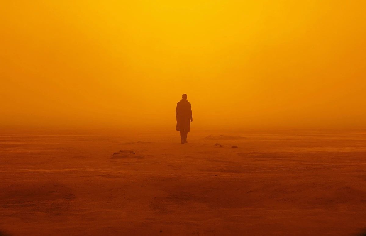 A lone silhouetted figure walking across a vast flat desert consumed entirely by a dense orange haze, in deep orange and red