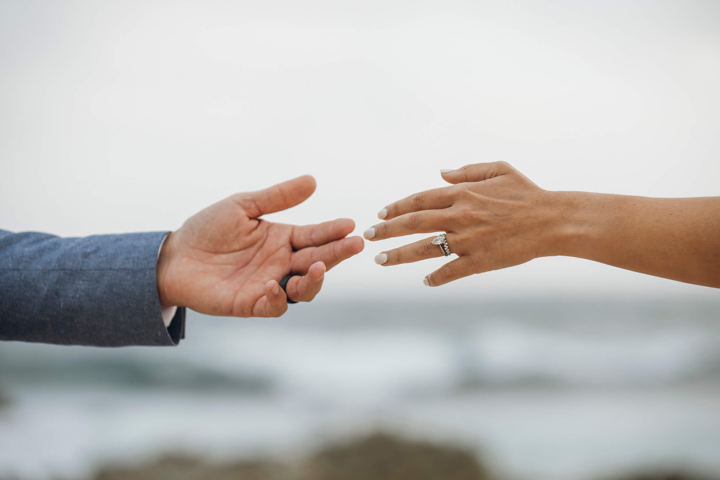 Creative close-up of bride and groom hands reaching toward each other at beach wedding