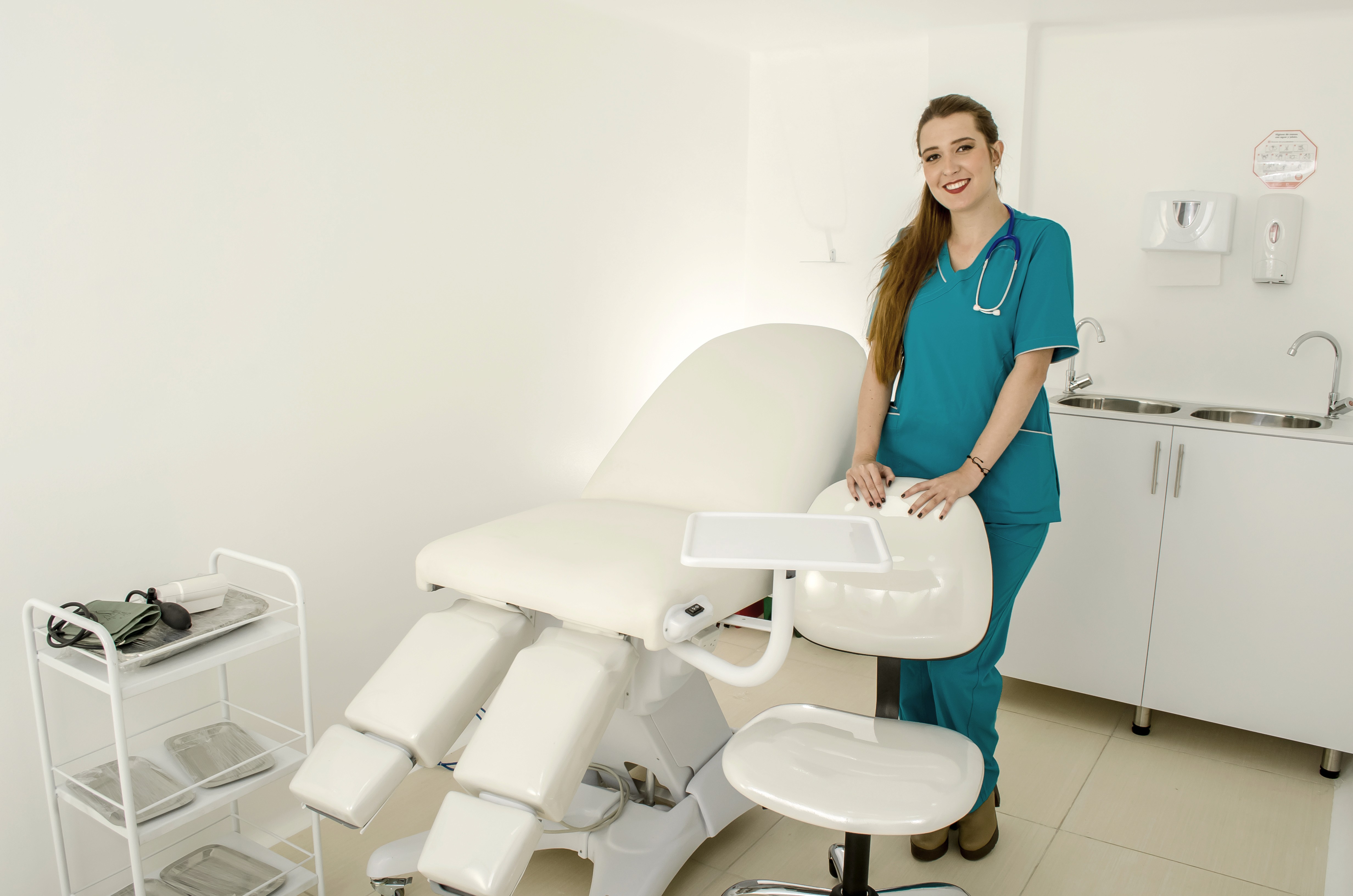 Auxiliar de enfermería en sala de procedimientos clínicos con camilla y equipo médico