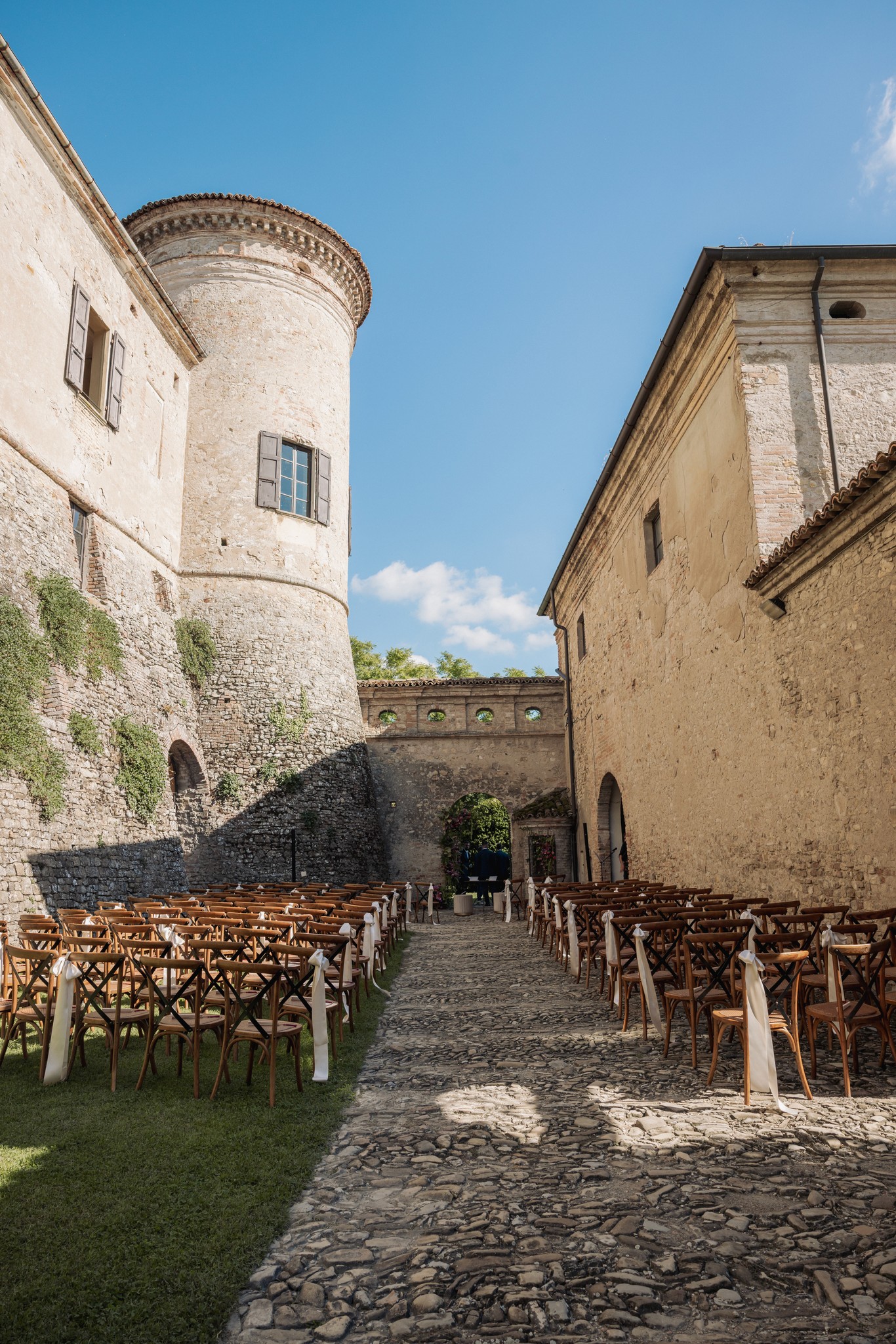 Cortile del Castello di Scipione allestito per cerimonia matrimoniale, sedie in legno e torre medievale sotto cielo sereno