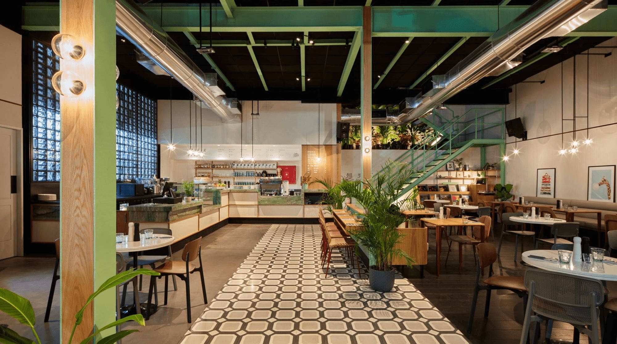 A breakfast place in Dubai that features a green theme with modern aesthetics, wooden seating and tables, greenery, and an open cafe setup.