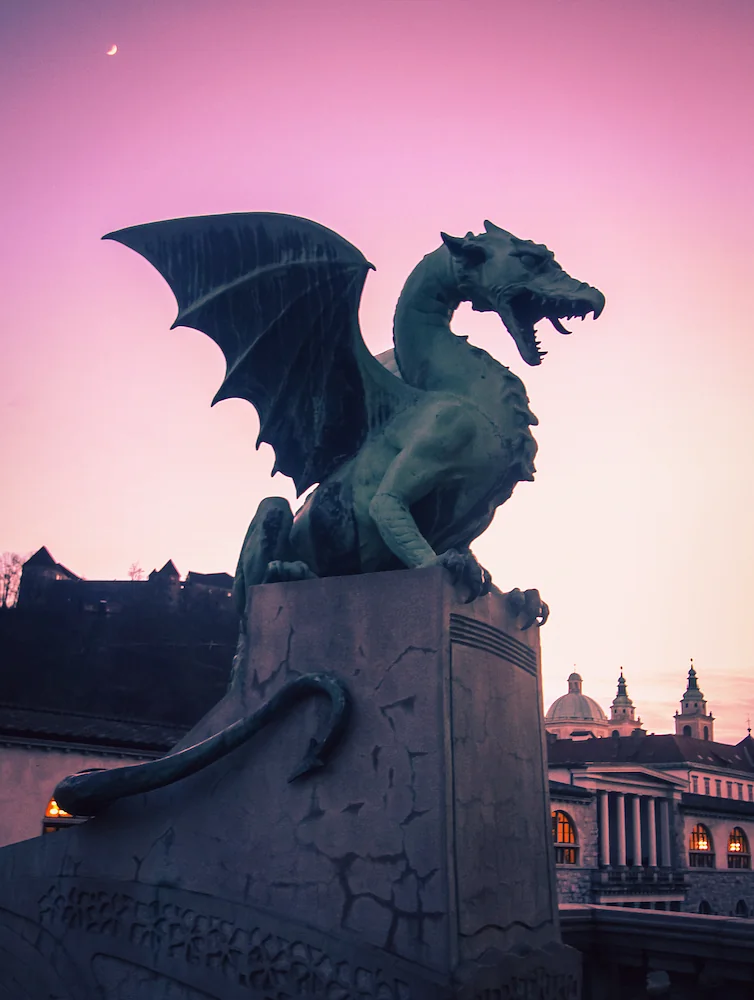 A statue of a dragon in Ljubljana center, below a pink colored sky.