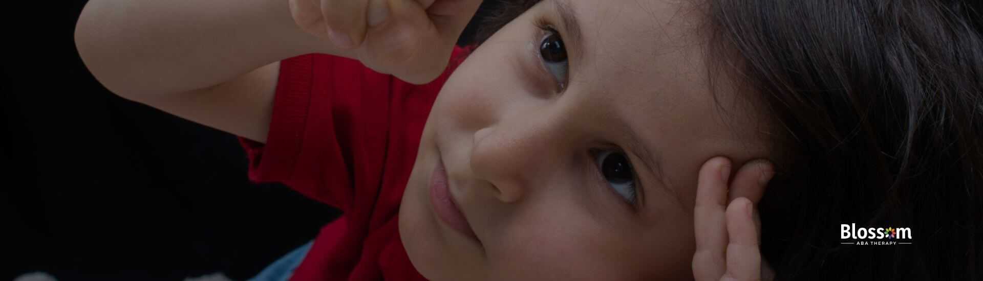 Close-up of a young child with autism pointing upward while looking attentively.
