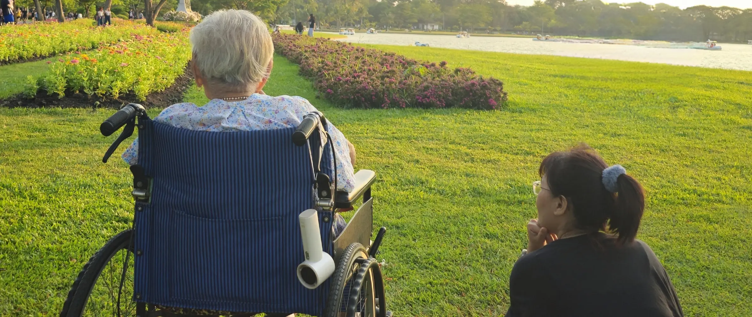 A caregiver sitting beside an older adult in a wheelchair, both looking out over a peaceful garden together in warm evening light.