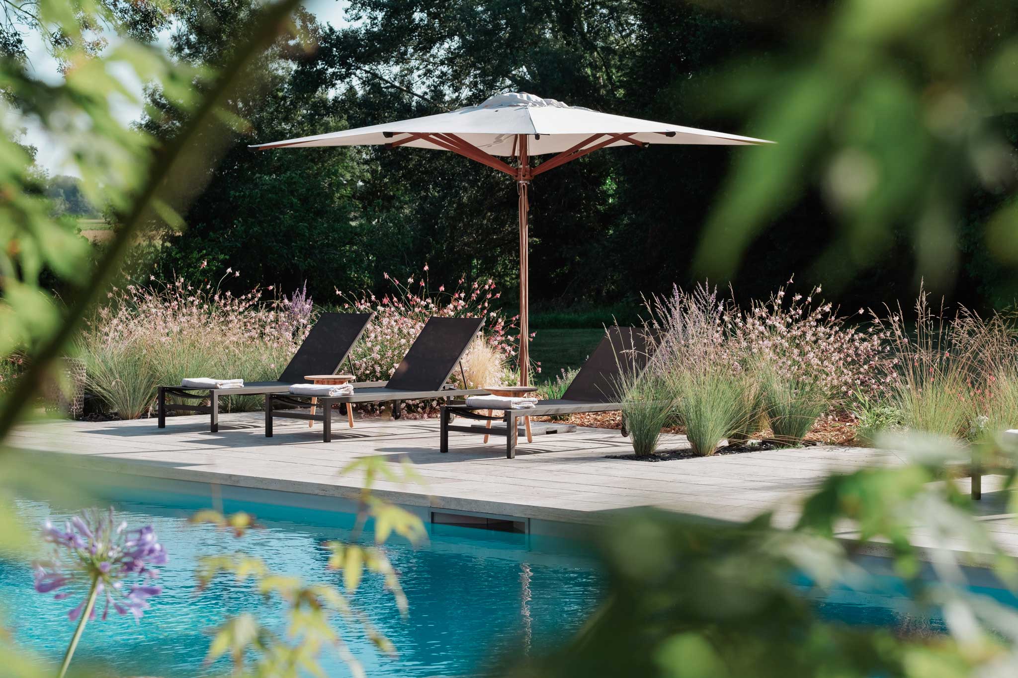 Espace détente extérieur avec piscine, transats et parasol, entouré de végétation naturelle, conçu par Invivo Paysage