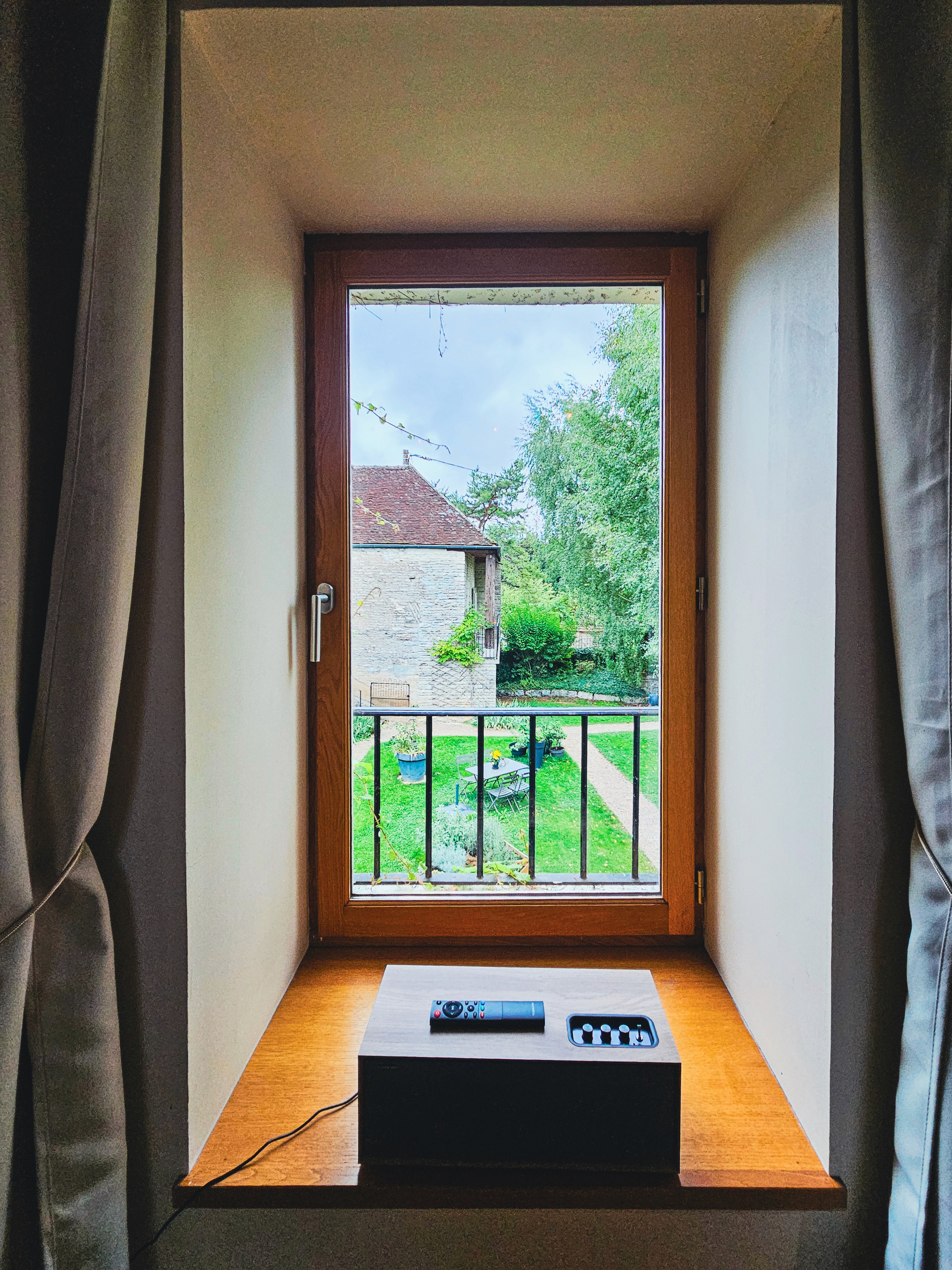 Fenêtre avec vue sur jardin verdoyant et maison ancienne. Paysage calme et serein.