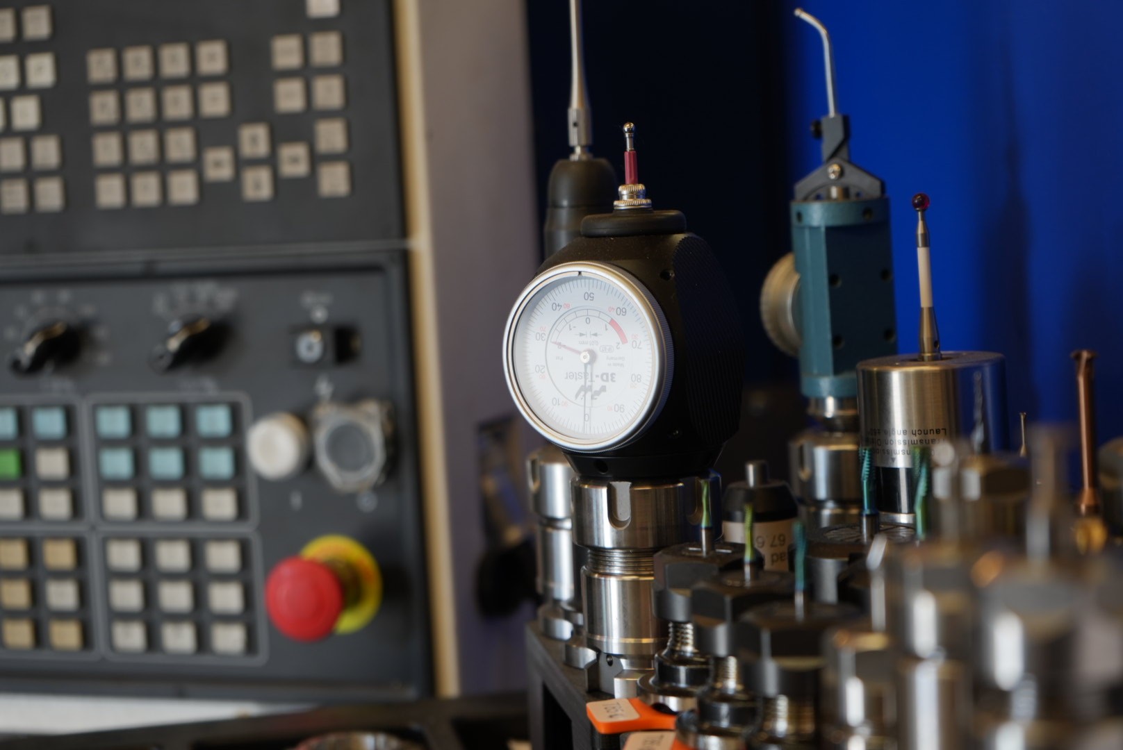 Modern architectural workspace with large floor-to-ceiling windows, surrounded by trees, and desks filled with design materials and books. Two blurred figures are walking through the space.