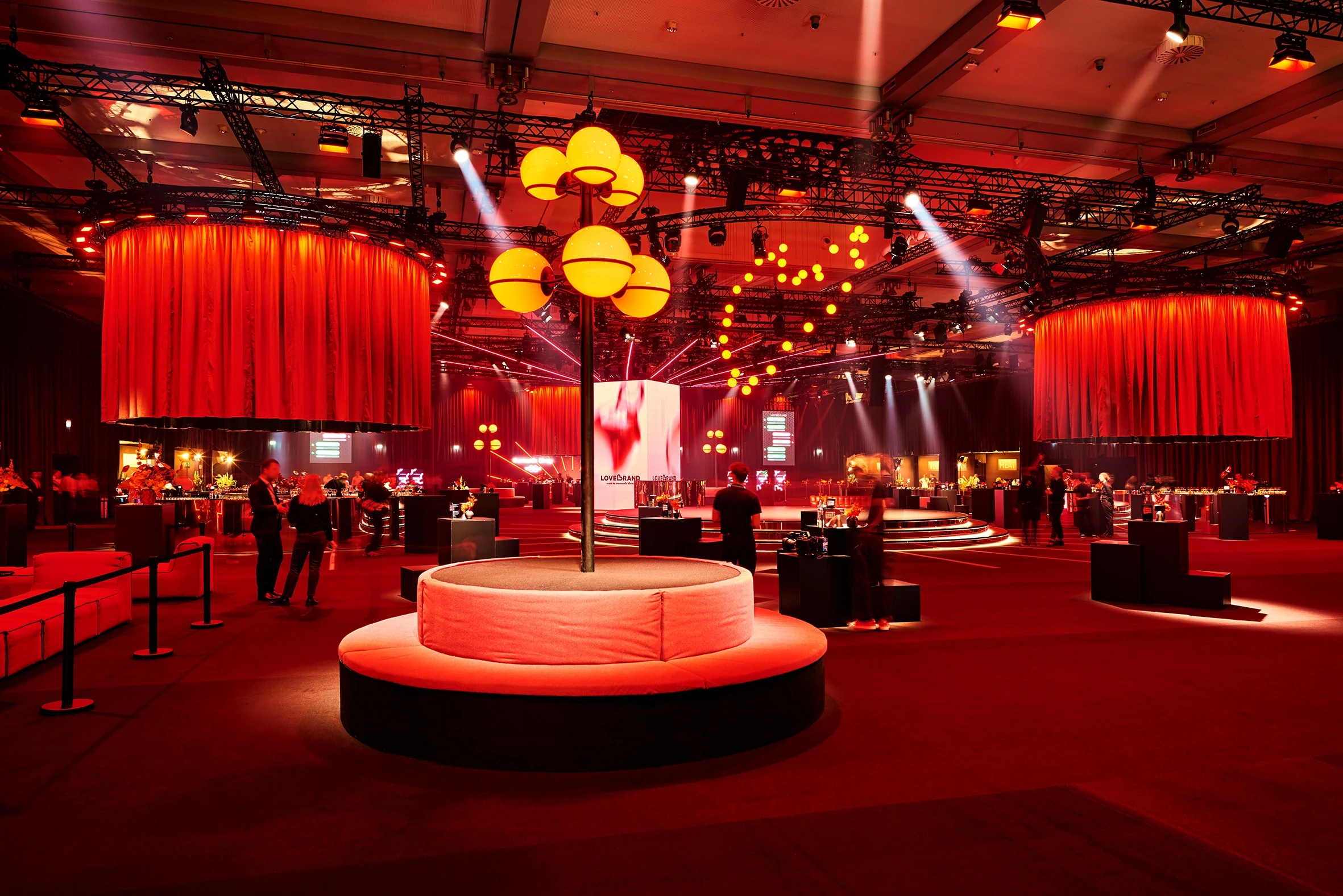Red ballroom with curtain cylinders, glowing lantern pillar and round upholstered benches.