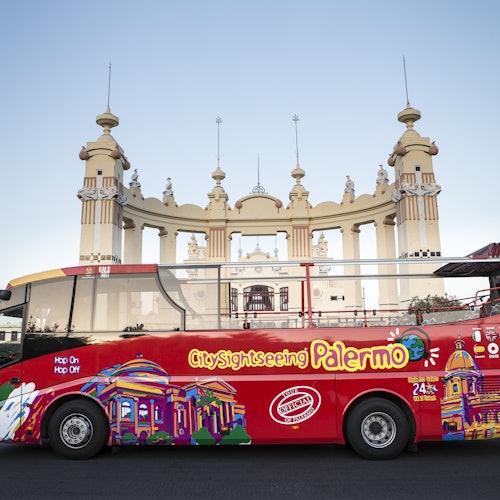 色鮮やかな都市観光バス「パレルモ」が、多くの塔を持つ華やかな歴史的建物の前に停められています。