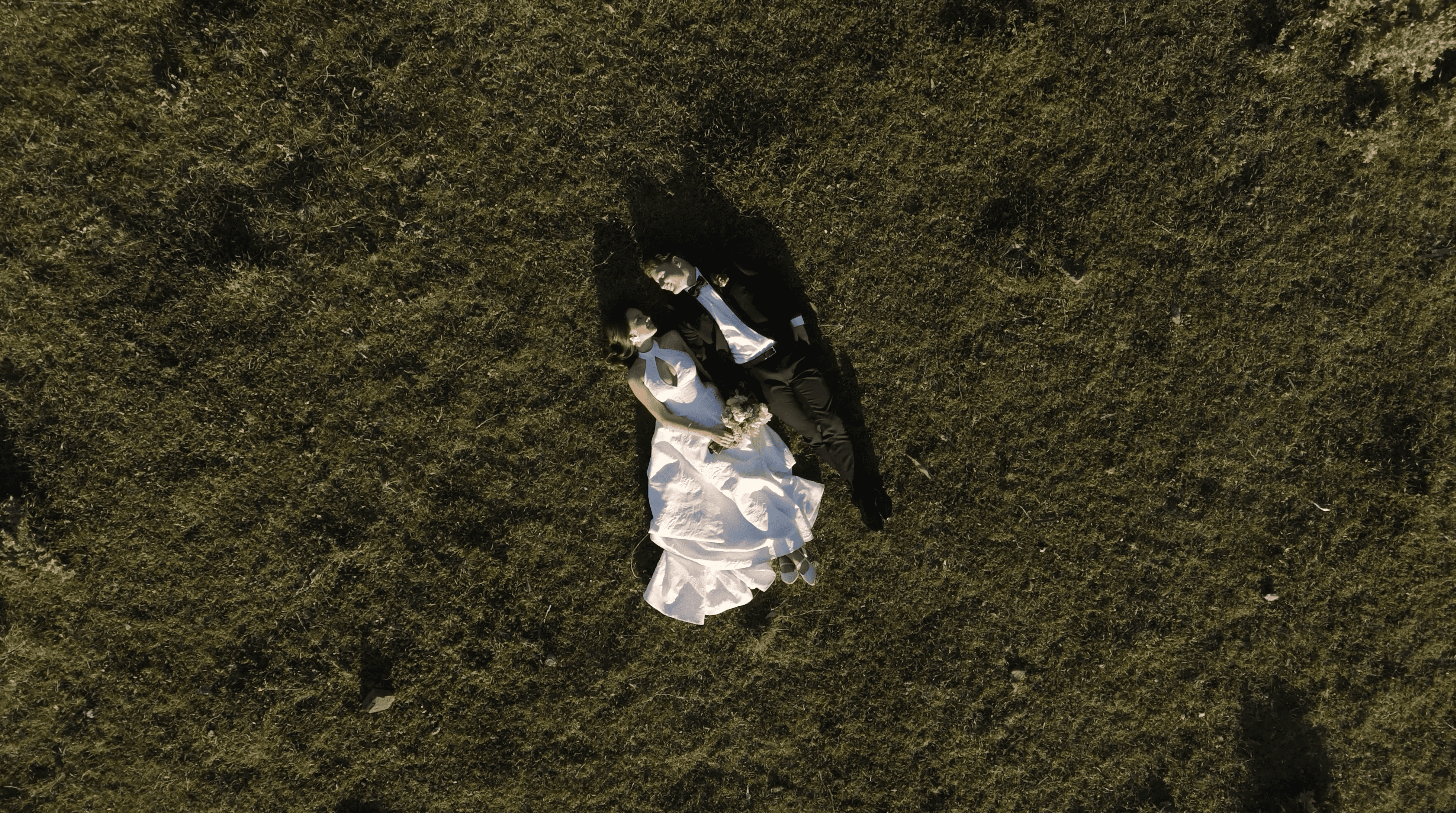 A joyful bride and groom walk hand in hand under a shower of white petals, surrounded by well-wishers and a sunny, blue sky.
