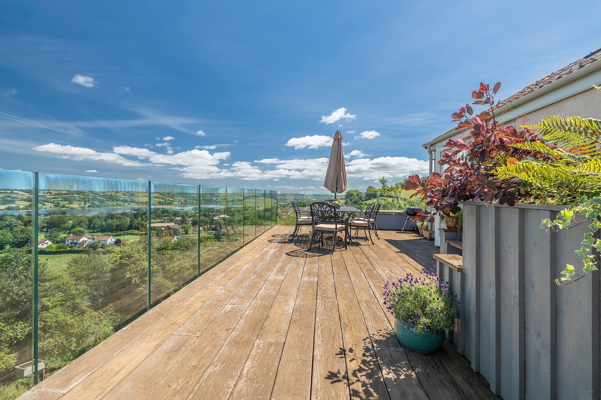 Wraparound decked terrace with glass balustrade and dining set, looking across to Blagdon Lake