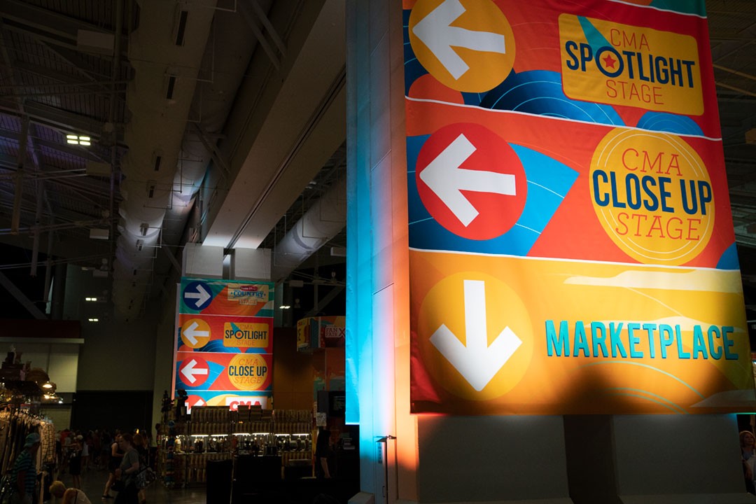 Directional signage inside the CMA Fest convention area guiding attendees to the Spotlight Stage, Close Up Stage, and Marketplace, enhancing wayfinding and branded fan experience.