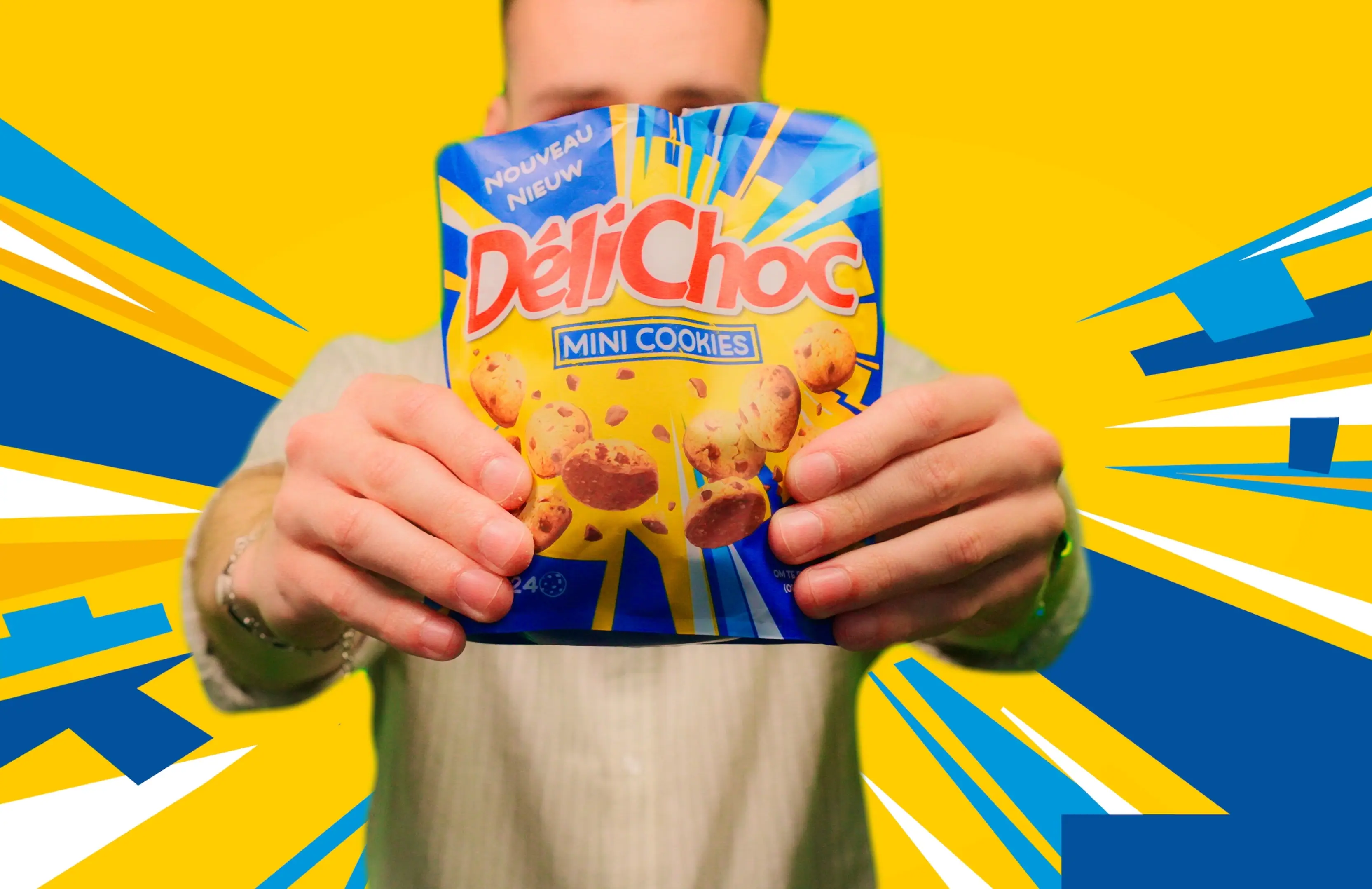 A person holds a vibrant package of DeliChoc Mini Cookies against a striking yellow and blue background, with dynamic graphic elements radiating outward to emphasize the product.