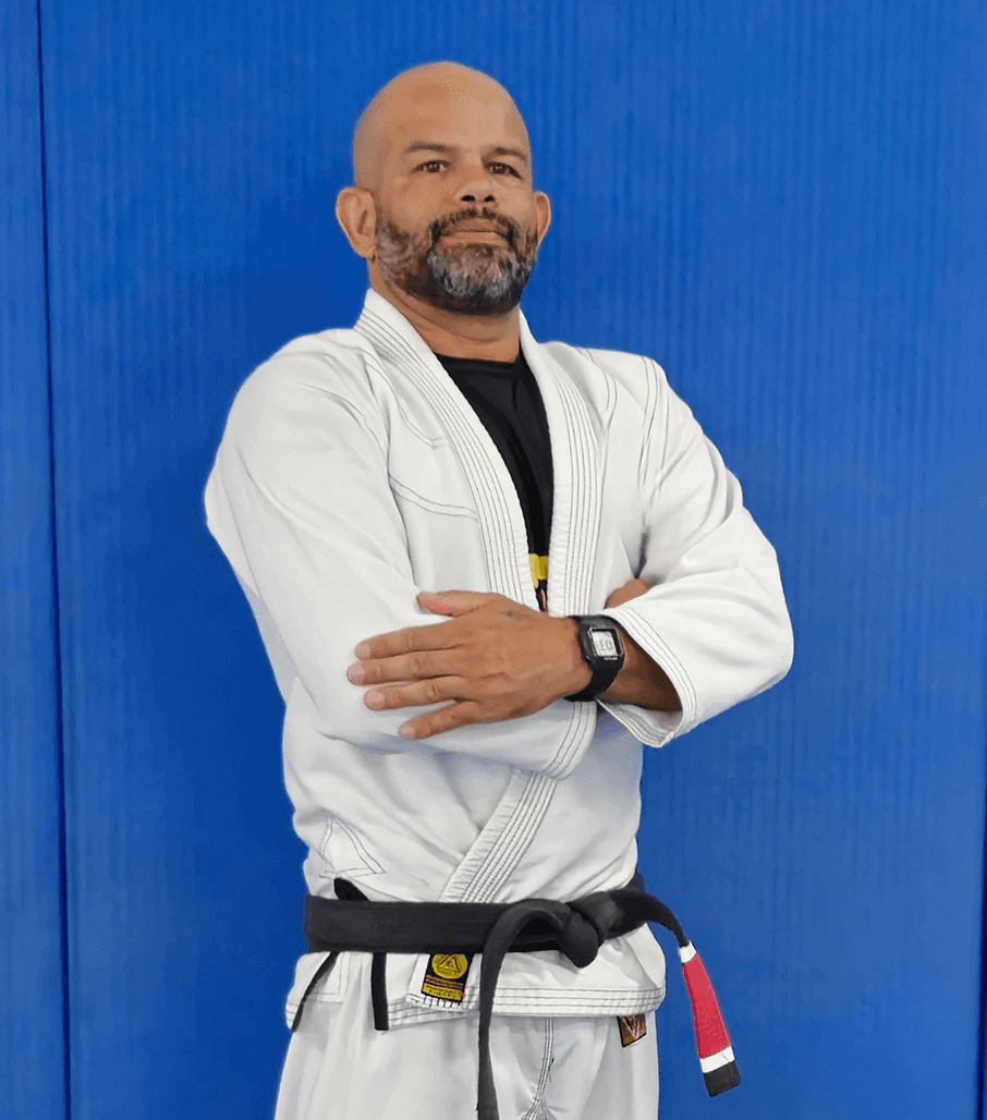 Tony “Ourico” in a white gi, arms crossed, standing confidently in front of a blue background