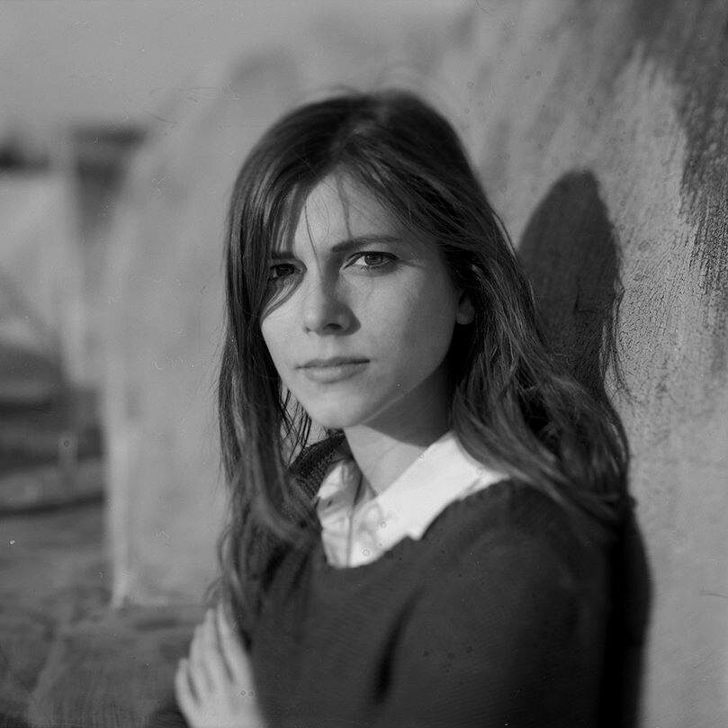 A thoughtful young person with dark hair gazes to the side, captured in soft black and white lighting.