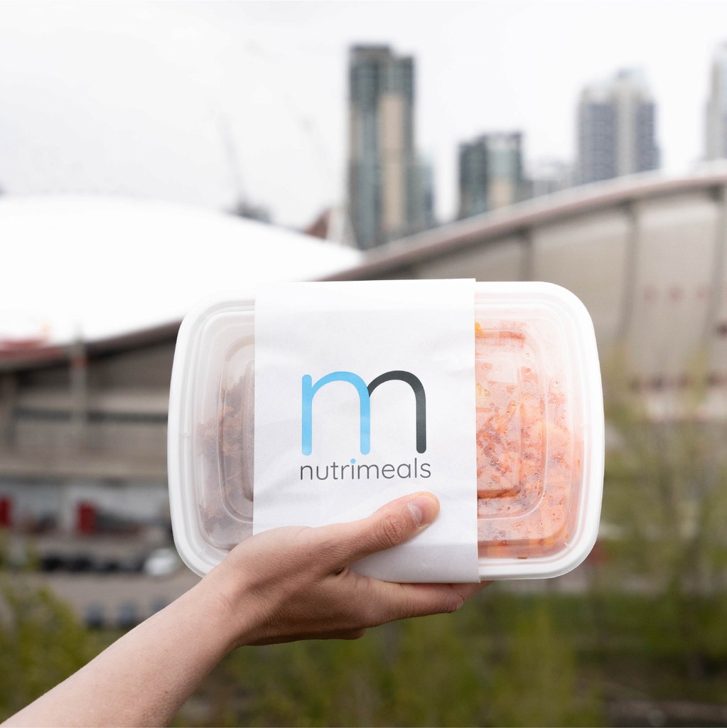 Image of someone holding a Nutrimeals meal in-front of downtown Calgary