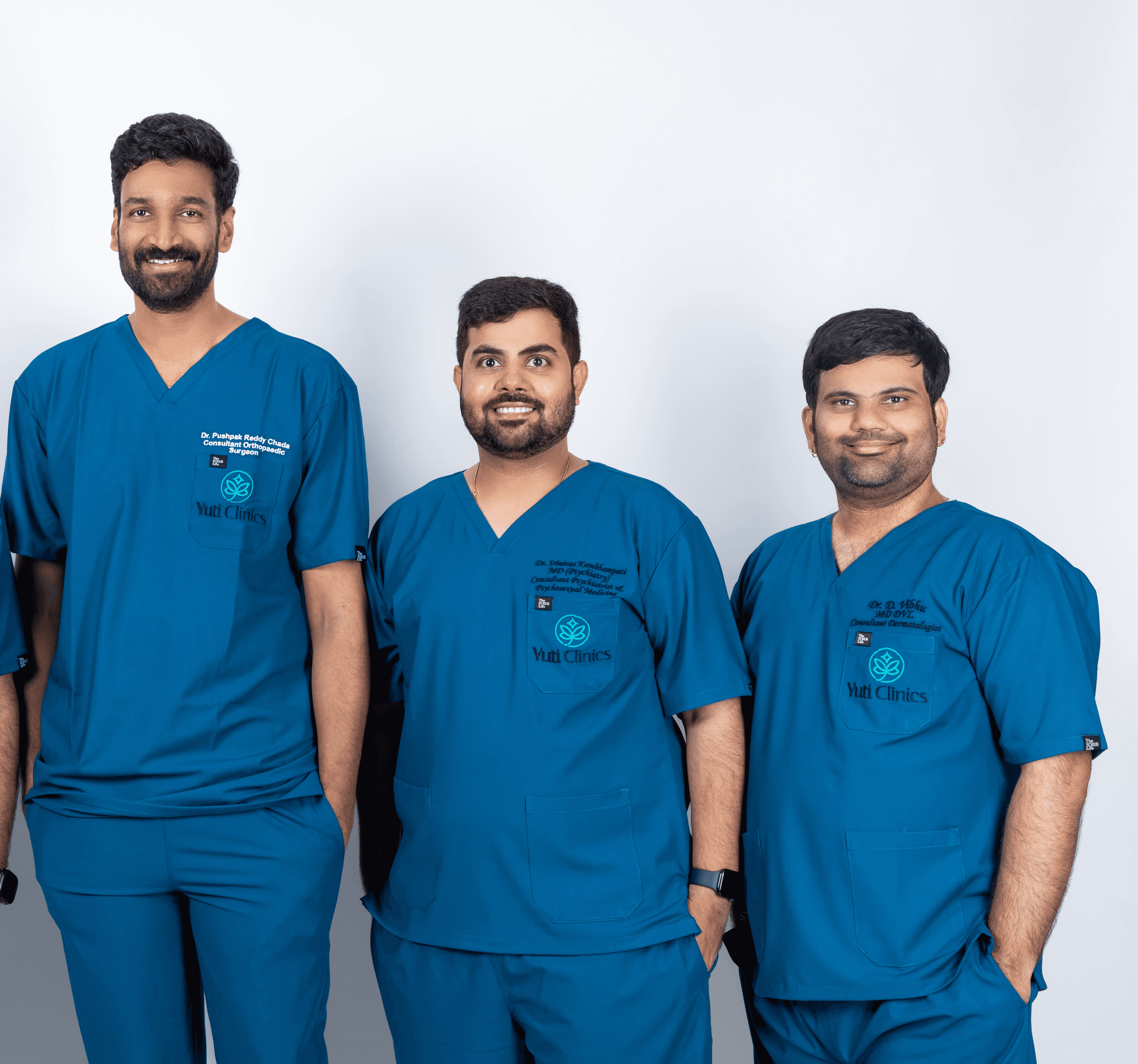 A young person with curly hair smiles at the camera while sitting in front of a laptop against a dark background.
