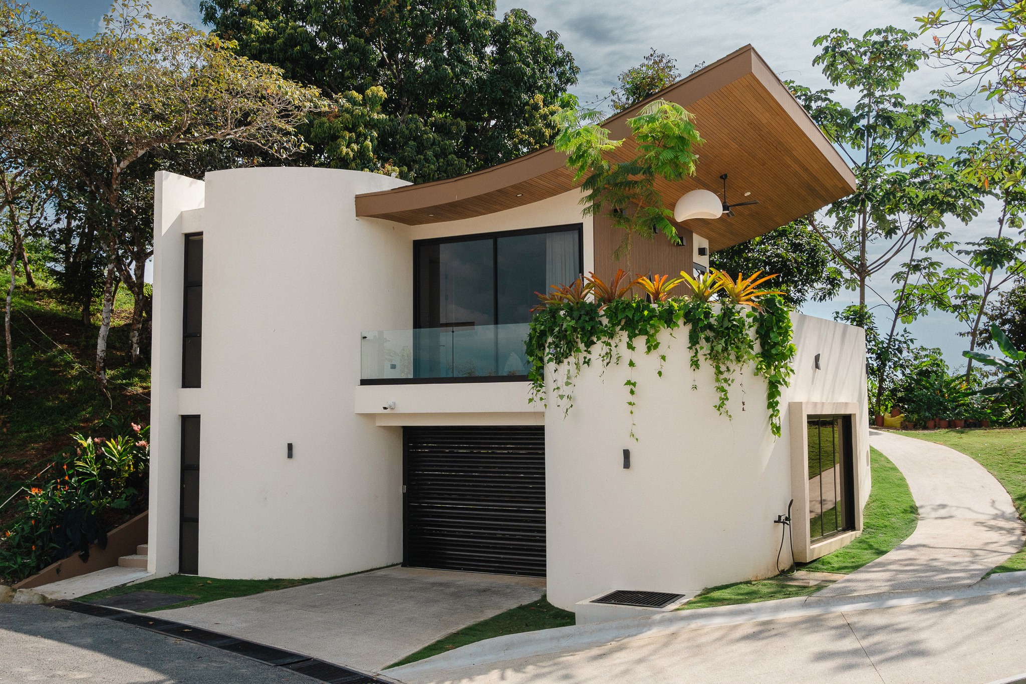Exterior view of a modern luxury casita in Manuel Antonio, Costa Rica featuring a unique curved white facade and a dramatic cantilevered wood ceiling.