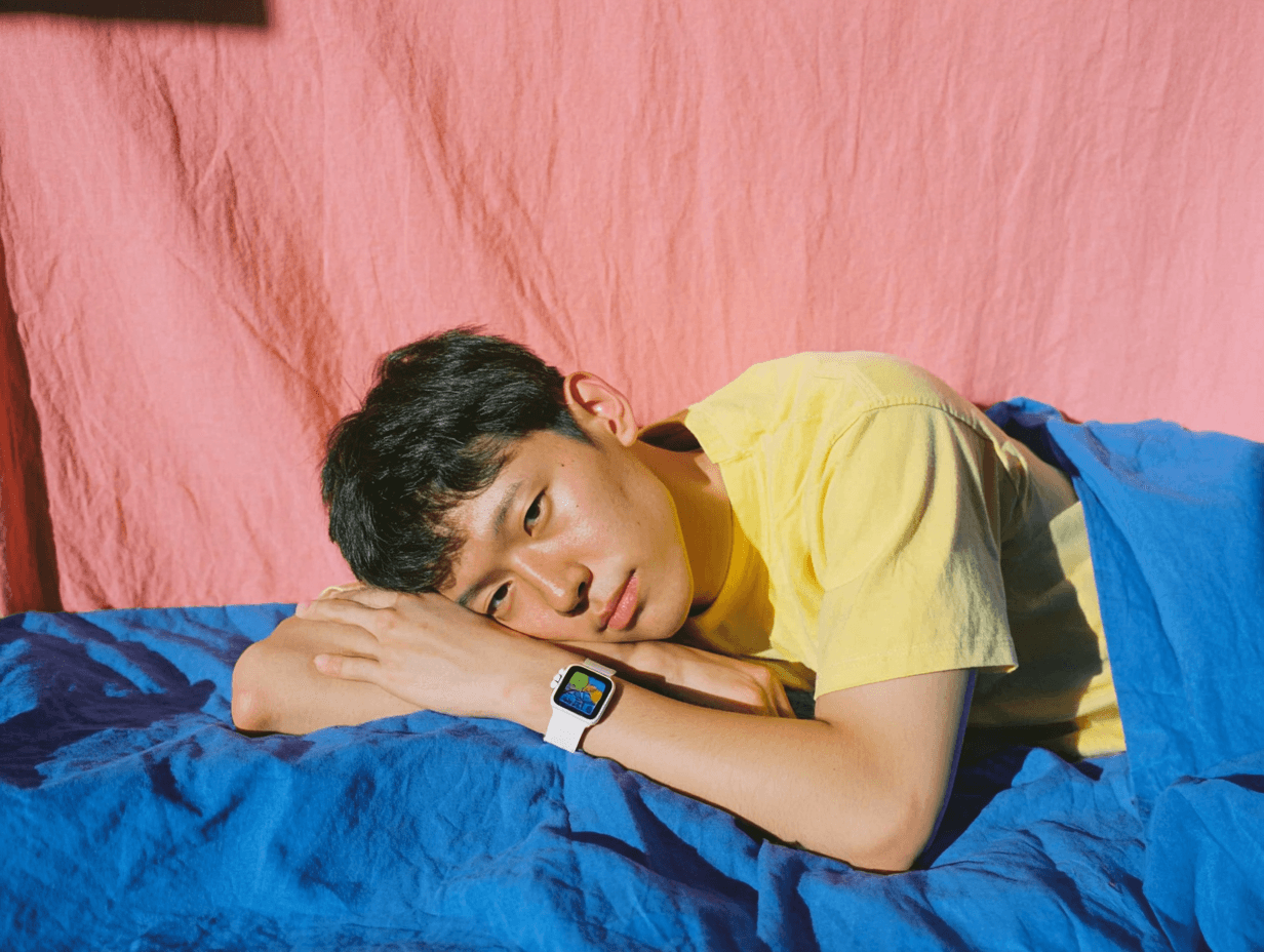A person in a yellow shirt wearing a smartwatch and resting on blue bedding during a break