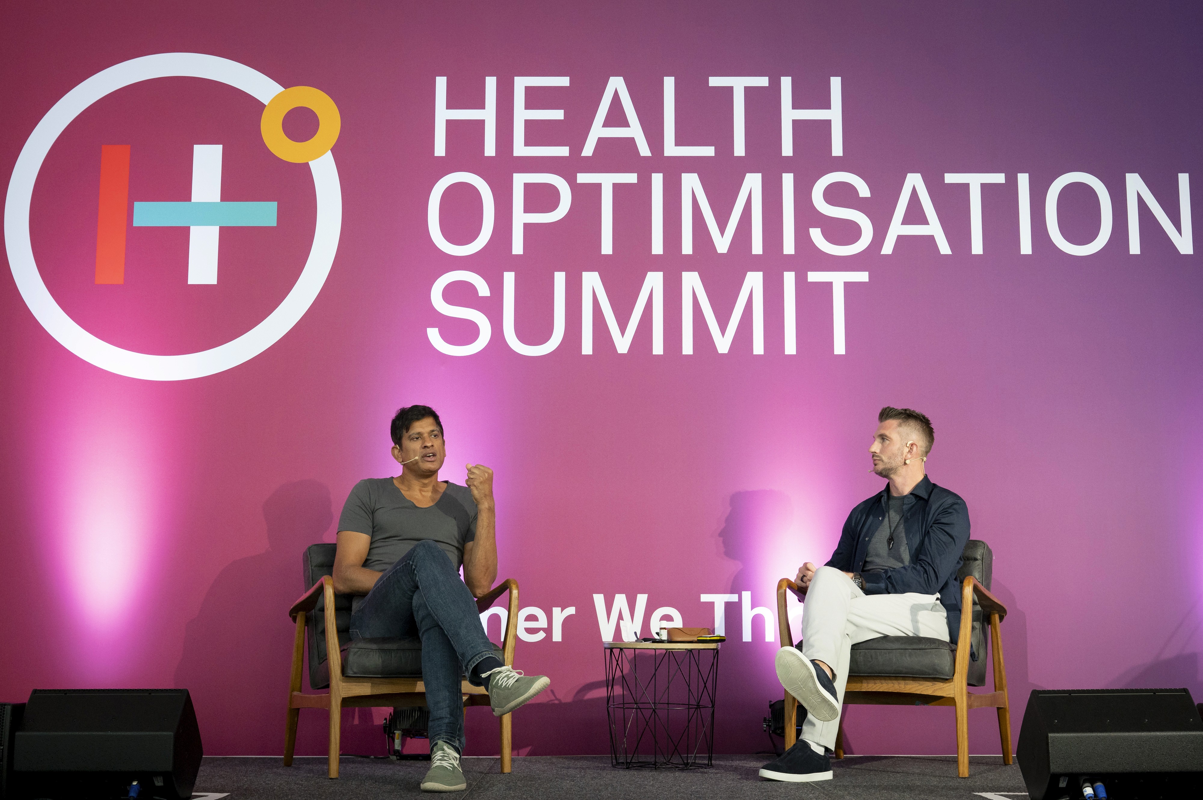 Group of hikers walking through a mountain meadow surrounded by pine trees and misty peaks.