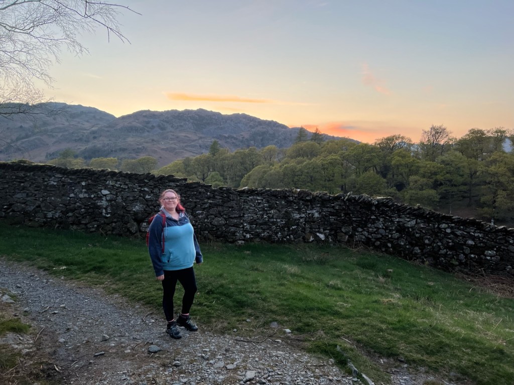 April walking down the path next to a stone dry wall. Fells in the background with the blue-hour sky.