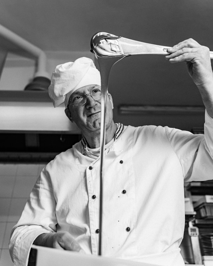 Black and white photo of a pastry chef drizzling chocolate from a spatula