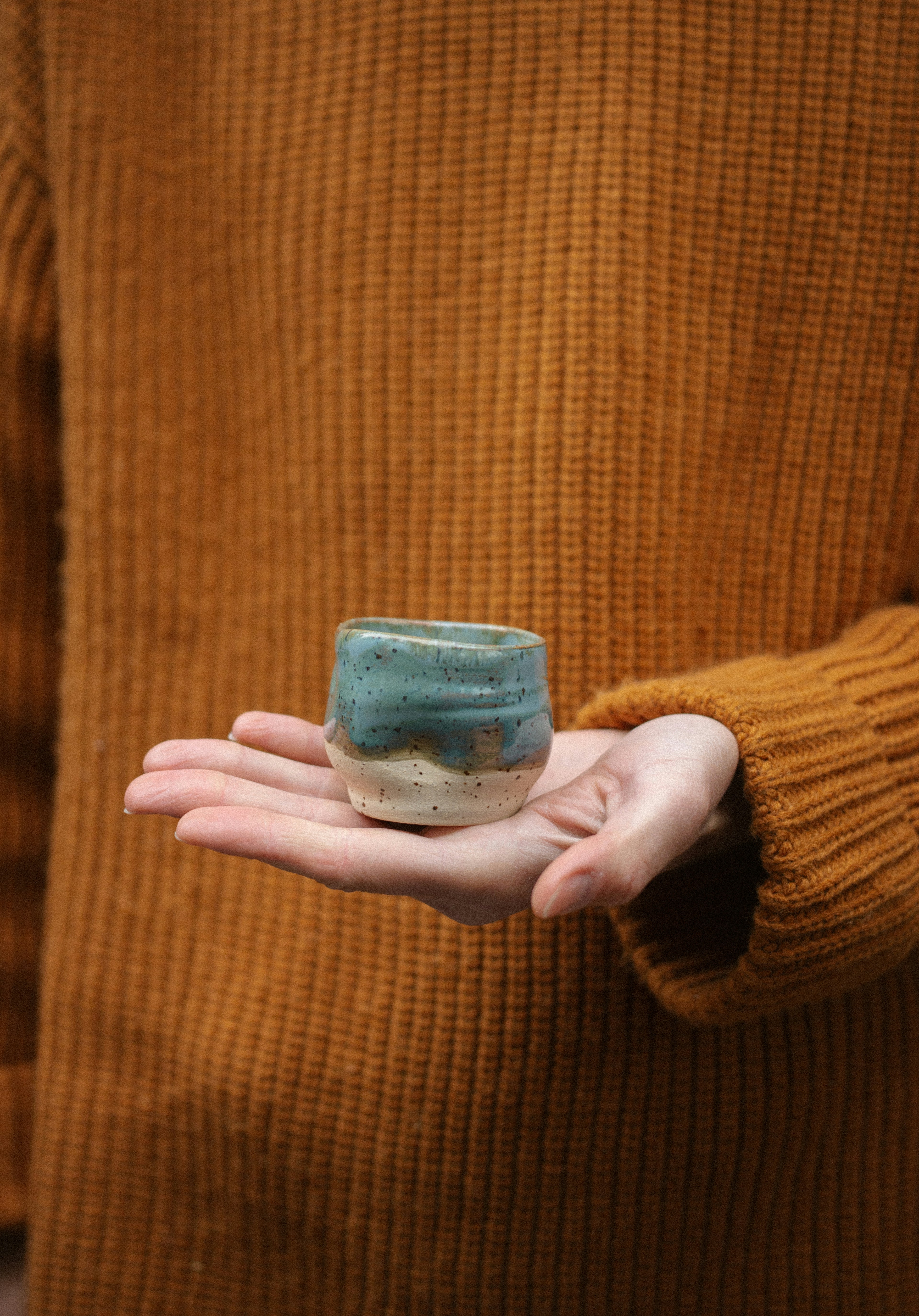 Hand holding a small, handcrafted ceramic cup.