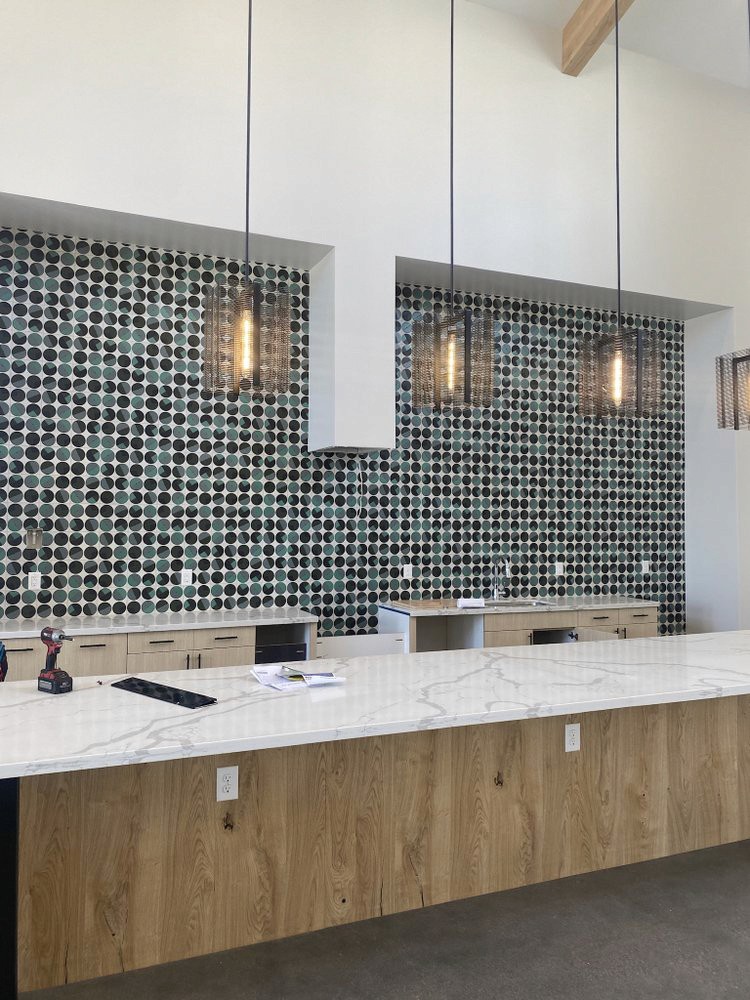 Modern kitchen with a white marble countertop, wooden base cabinets, and a black and green dotted tile backsplash, featuring three hanging pendant lights.