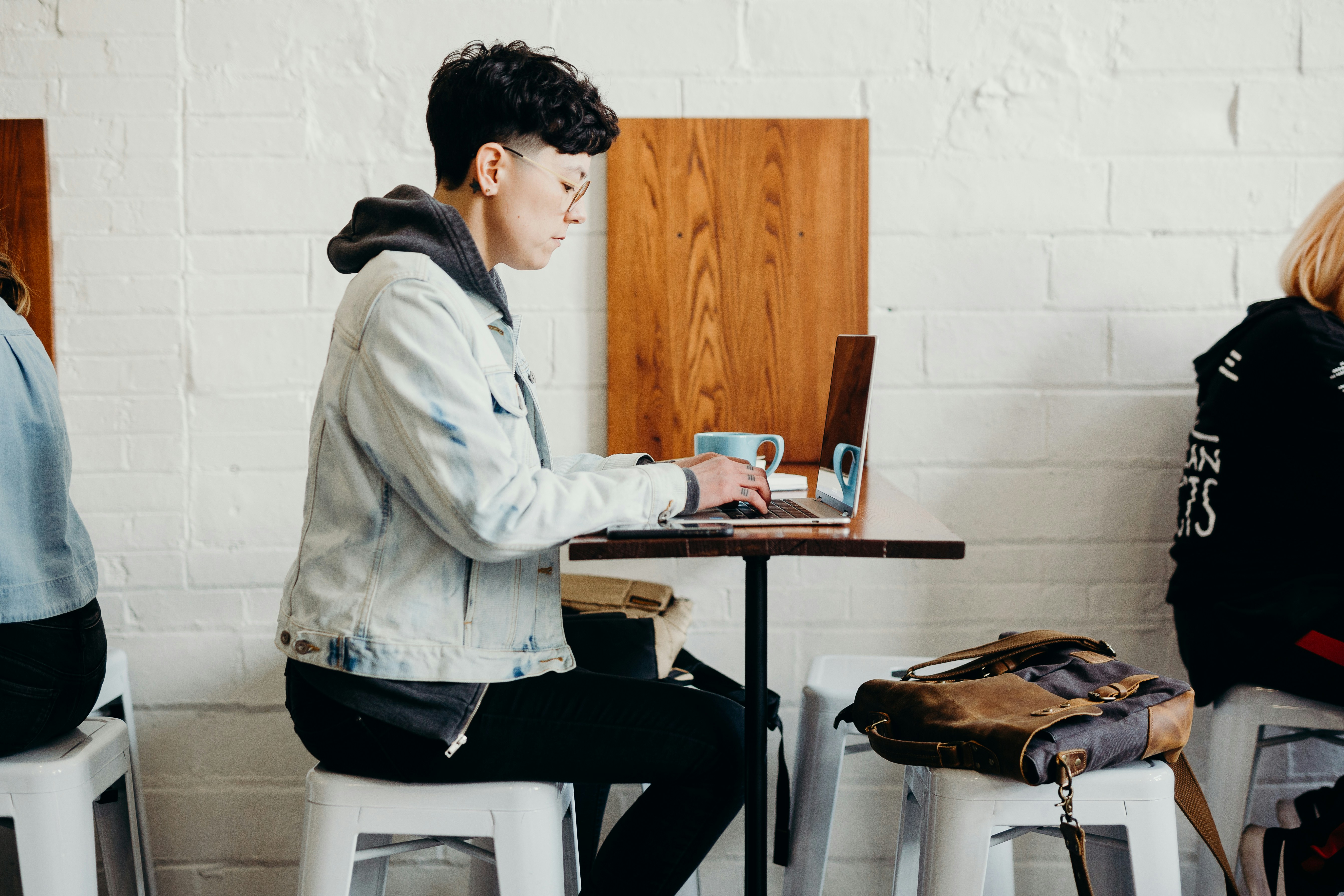 A man in a cafe is sat using his laptop whilst drinking coffee.