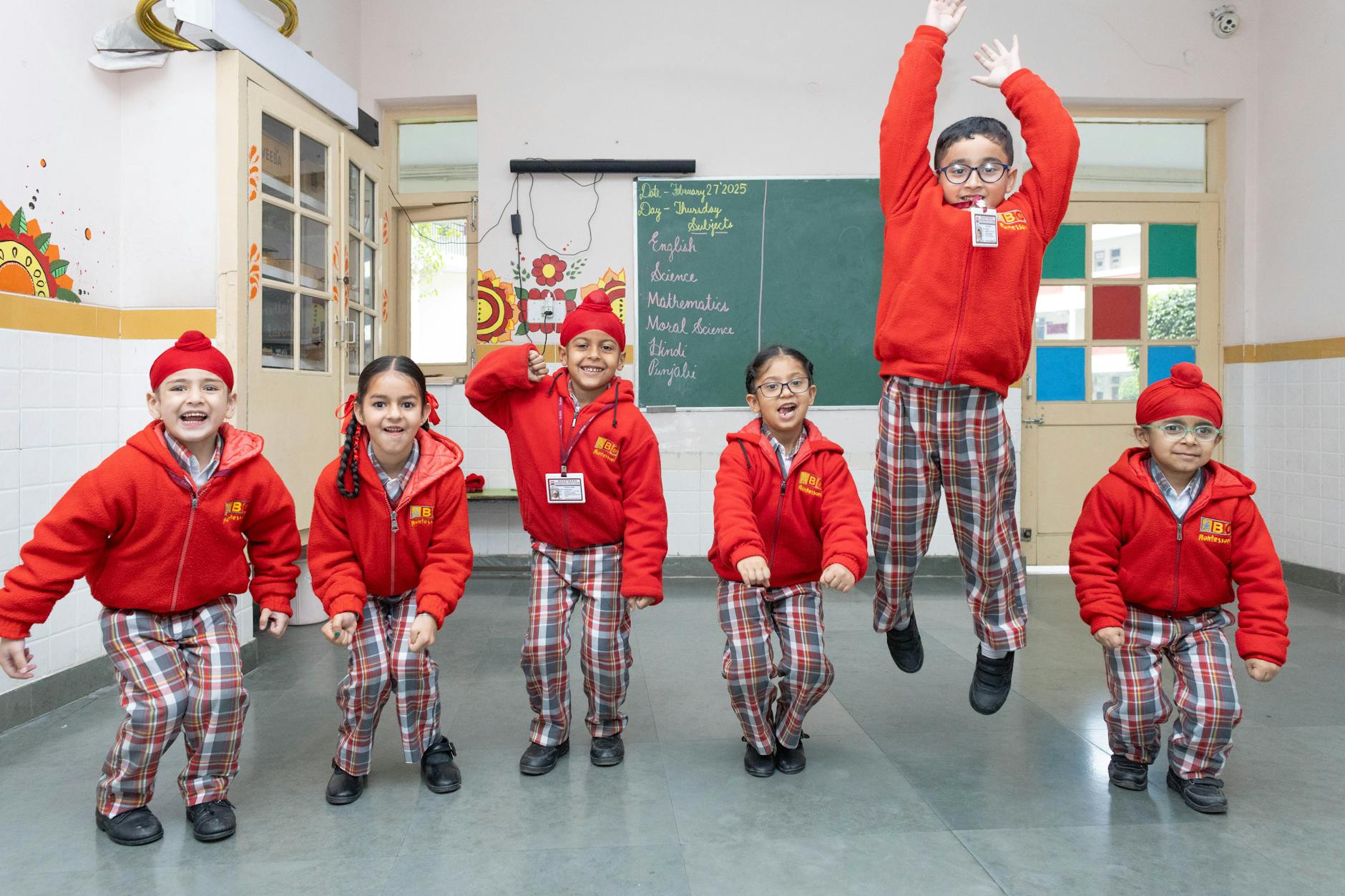 A group of energetic children standing by their desks following a dance routine projected on a large screen.