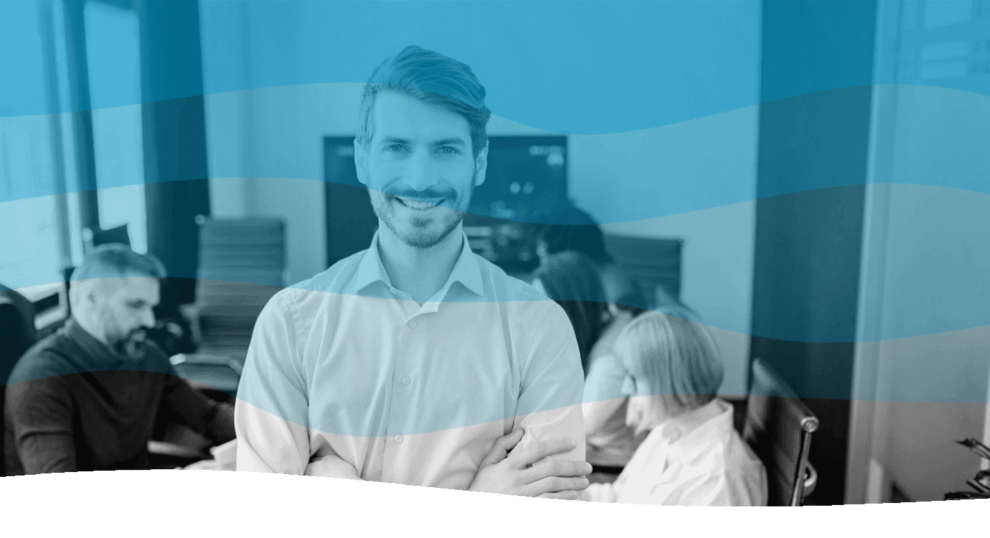 A man in a bright office stands confidently in the foreground, with colleagues collaborating at a desk behind him.