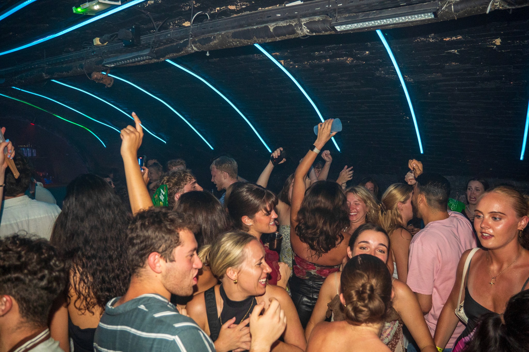 Crowded dance floor inside a nightclub during a bar crawl in Nice with people dancing arms raised loud music and neon lights capturing intense party energy collective excitement and the high volume nightlife atmosphere of a peak moment on the French Riviera