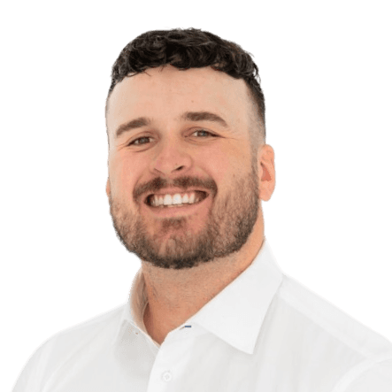 Professional headshot of a smiling man with short dark curly hair and a beard wearing a white collared shirt against a black background