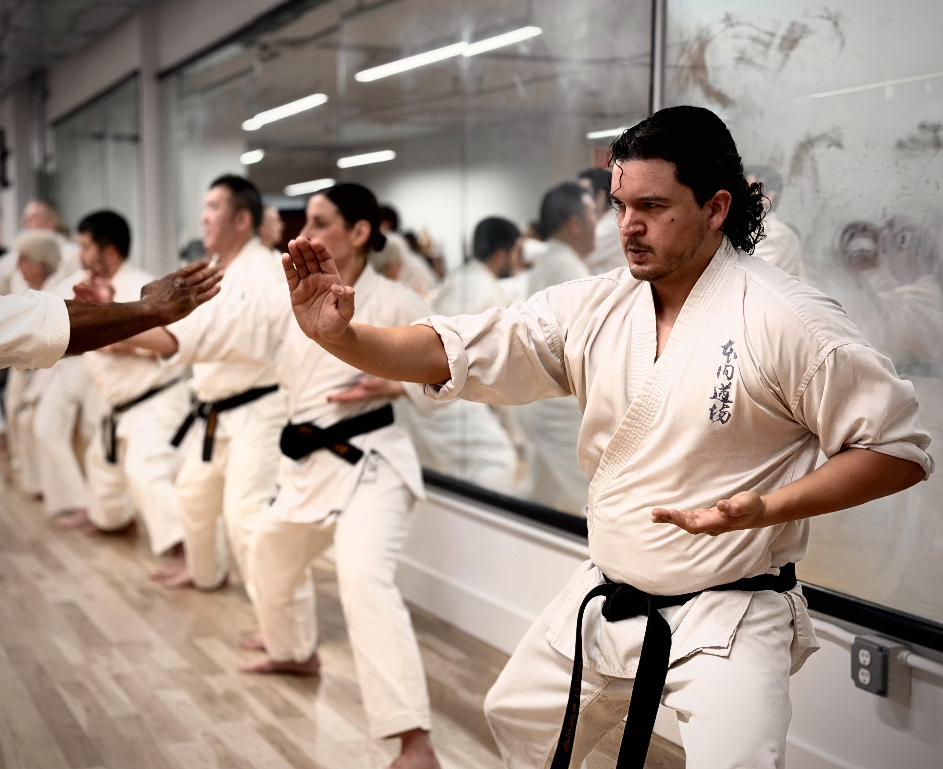 White plate with roasted carrots served on green sauce, topped with almonds and fresh herbs, held by a hand over a dark table.