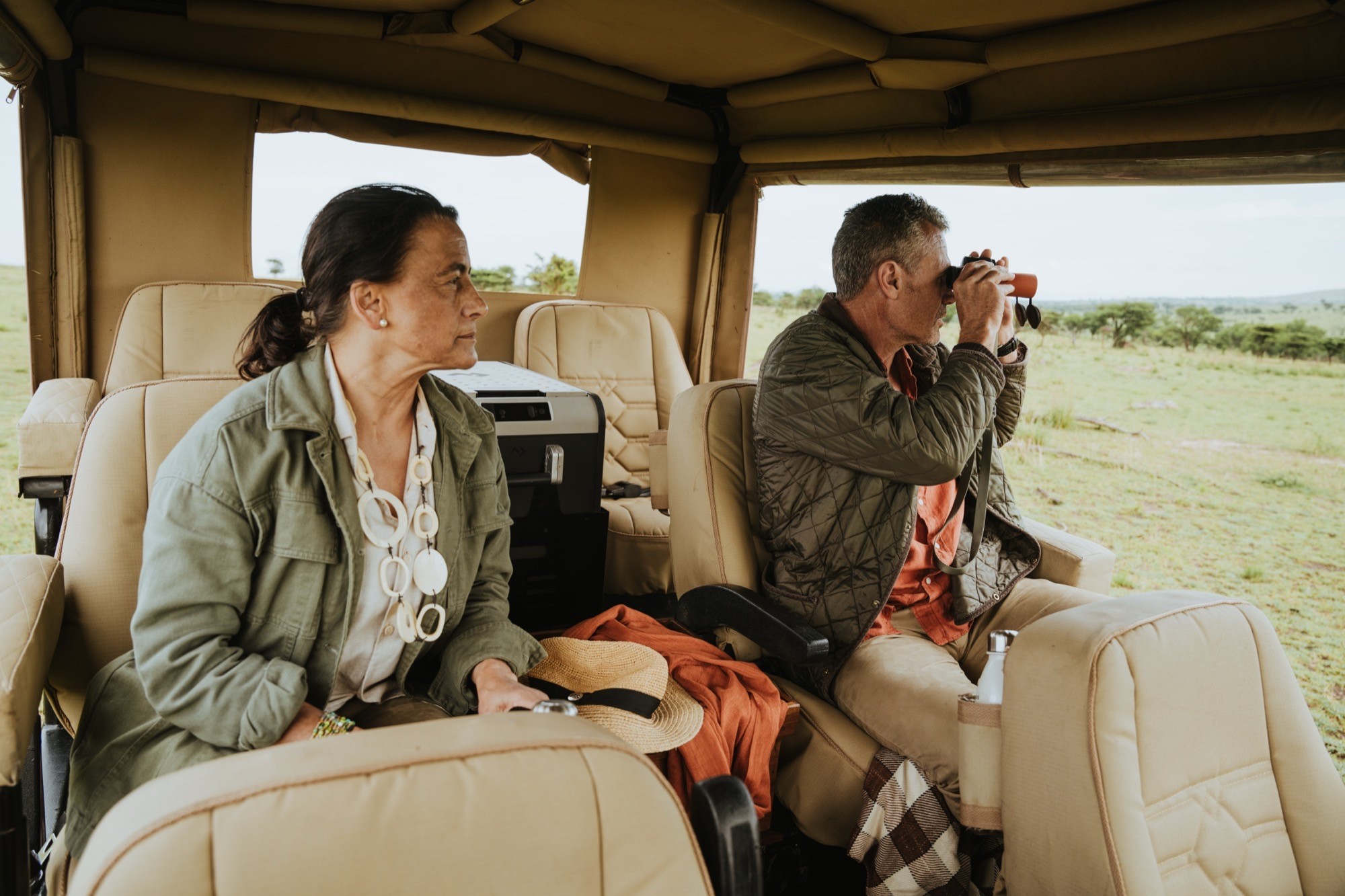 A couple scanning the plains with binoculars from an open game-drive vehicle