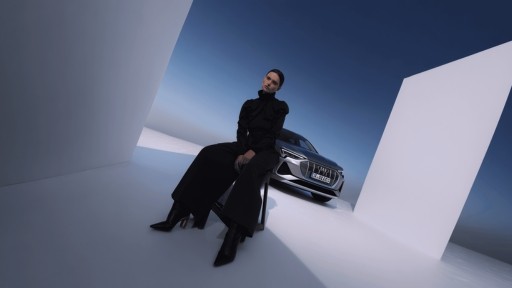 Eine Dame sitzt auf einem Hocker in einem Studio mit blauem Dach und im Hintergrund ein Fahrzeug