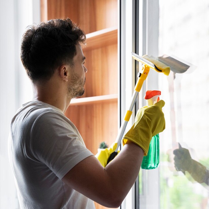 Un homme de dos s'applique pour nettoyer une vitre en plein jour à Morez