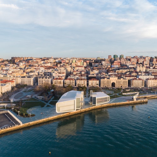 Aerial view of a coastal city with modern white buildings along a waterfront, dense urban area, and clear water.