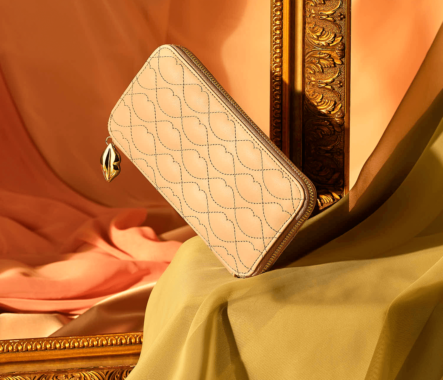 A soft pink wallet rests elegantly on a draped surface, with warm, textured backgrounds.