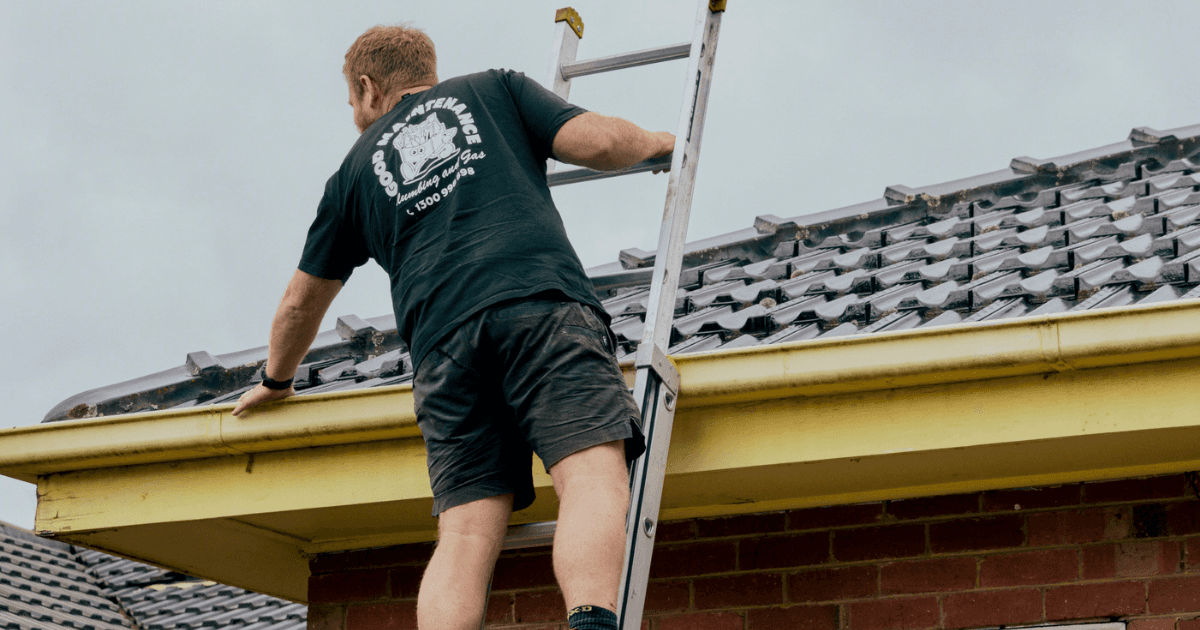 Good Maintenance Technition on a ladder checking the gutters on the roof of a residential house.