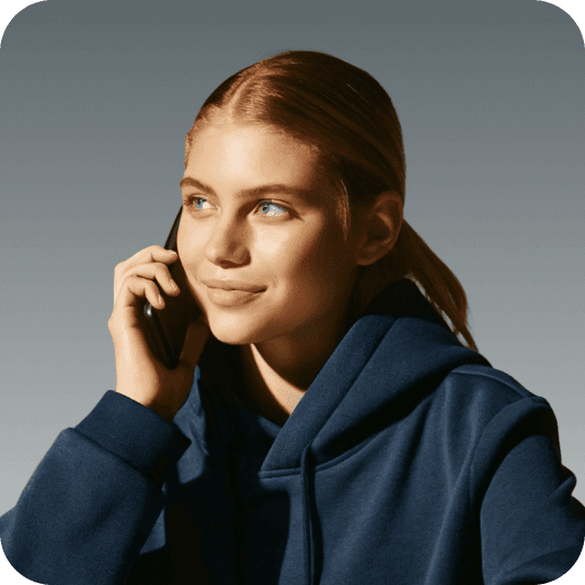 Smiling young woman in a navy hoodie holding a phone to her ear and looking left