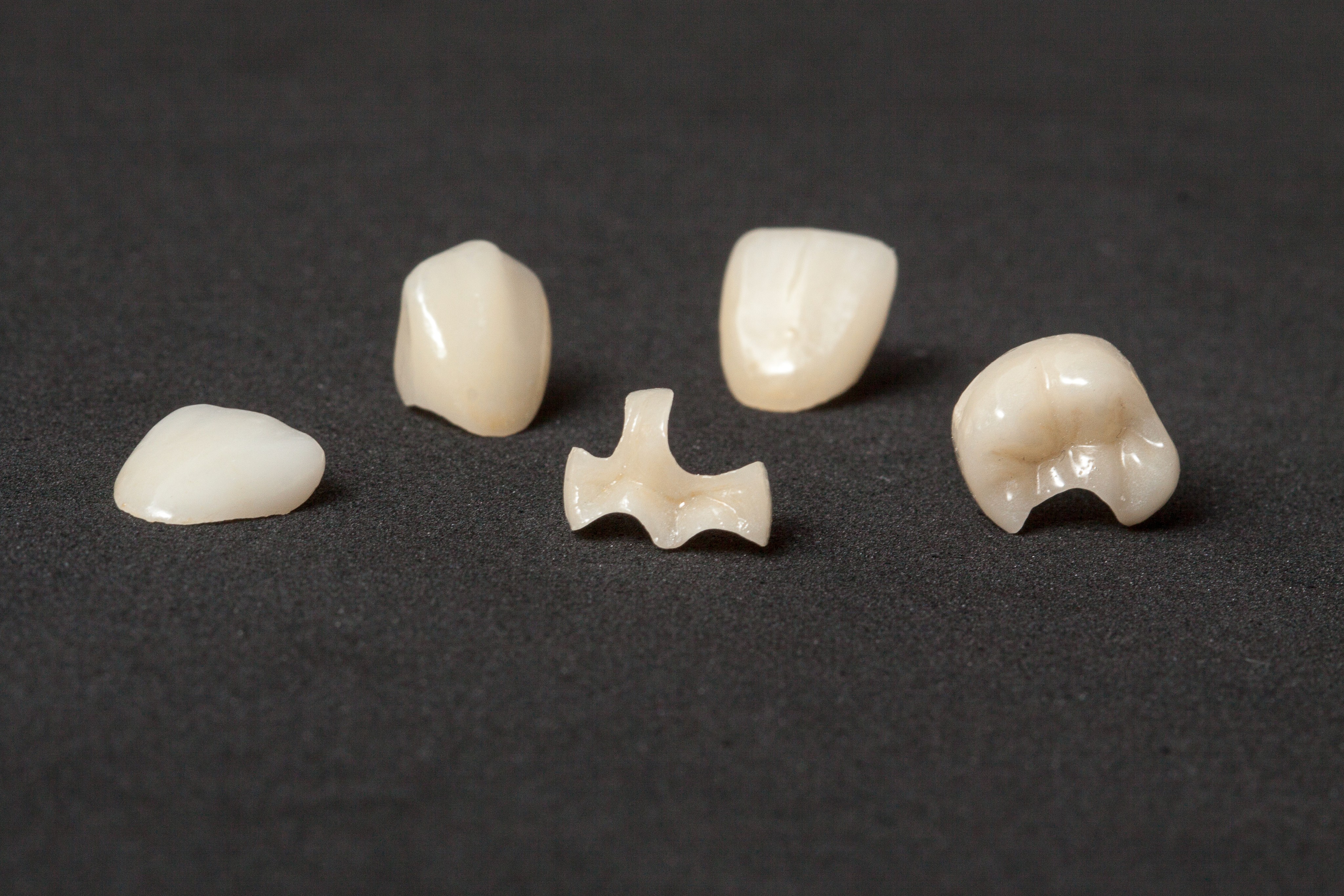 Ceramic dental crowns and bridges are displayed on a dark surface, showcasing a variety of shapes and sizes, highlighting options for restorative dentistry solutions.