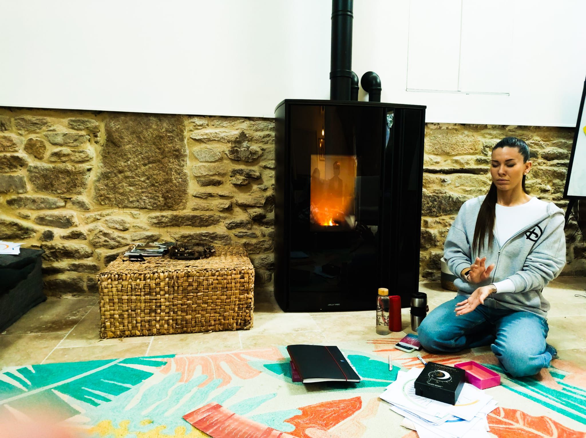 Wooden sauna cabin and hot tub set among rocky mountains and greenery under clear sky.