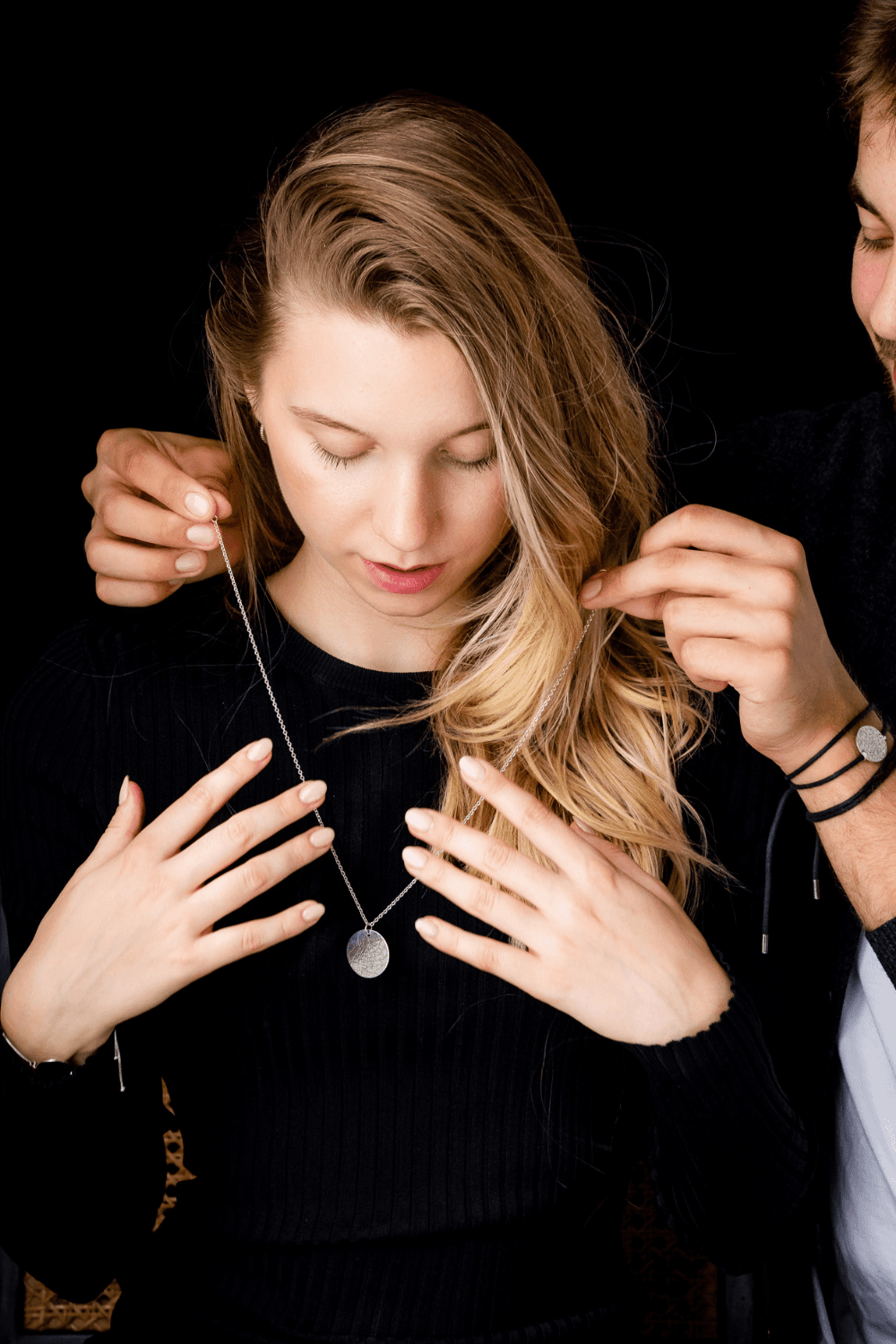 A man wearing a Night Sky Star Map bracelet is putting a Night Sky Star Map necklace around a woman's neck. 