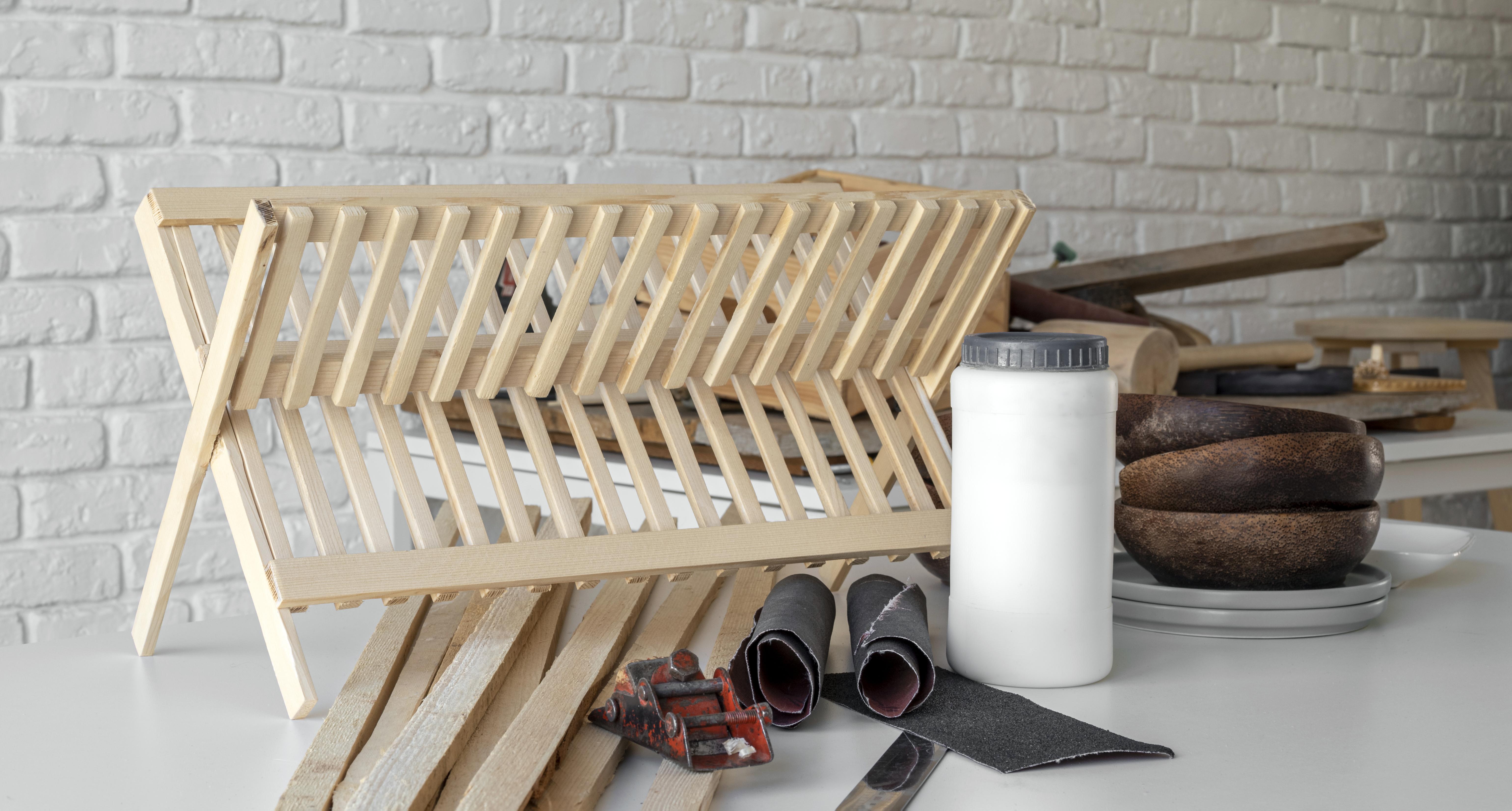 Wooden dish rack, glue, sandpaper, and wooden bowls on a white table. DIY woodworking project.